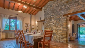 A dining area with a stone wall, wooden ceiling beams, and a tiled floor.