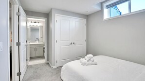A bedroom with a large bed, a closet with a mirror, and a bathroom with a sink and vanity. - Family Retreat 2BDR 2BT / Remote Work Ready / Lake Access / Games / South Health (Calgary)