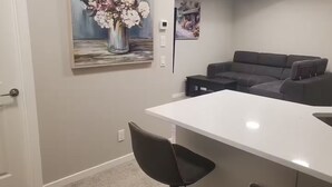A modern living room with a white dining table, a gray sofa, and a black chair. There are two paintings on the wall. - Family Retreat 2BDR 2BT / Remote Work Ready / Lake Access / Games / South Health (Calgary)