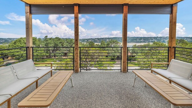 A covered outdoor seating area with two benches and a table, overlooking a scenic landscape with trees and buildings. - Lake Travis Retreat w/ Pool, Views & Outdoor Kitchen. Perfect for groups (Lago Vista)