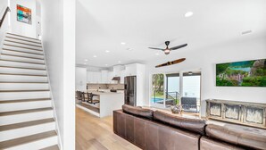 A modern kitchen with white cabinets, a central island, and a dining area with a brown leather couch. - Lake Travis Retreat w/ Pool, Views & Outdoor Kitchen. Perfect for groups (Lago Vista)