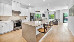 A modern kitchen with white cabinets, stainless steel appliances, and a large island with bar stools. - Lake Travis Retreat w/ Pool, Views & Outdoor Kitchen. Perfect for groups (Lago Vista)