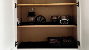Un meuble avec trois étagères, contenant un bocal étiqueté « Thé à la camomille », un bocal étiqueté « Sucre » et une boîte de « Malt’s Bakery Nutri ».