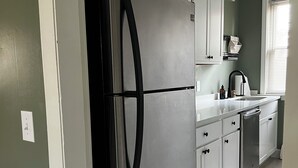 Une cuisine dotée d’un réfrigérateur en acier inoxydable, de meubles blancs et d’une fenêtre avec des stores.