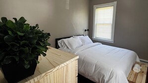 Une chambre à coucher avec un lit, une fenêtre, une plante en pot et une table de chevet en bois.