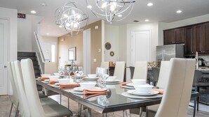 A modern dining area with a long table set for six, surrounded by chairs. There is a kitchen area with dark wooden cabinets and a stainless steel refrigerator. - Stunning 9BR/8.5BA Retreat with Private Pool & SPA-280CW (Kissimmee)