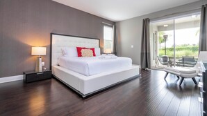 A modern hotel room with a large bed, a bedside table with a lamp, and a view of the outdoors through a sliding glass door. - Stunning 9BR/8.5BA Retreat with Private Pool & SPA-280CW (Kissimmee)