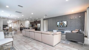 A modern living room with a sectional sofa, a grey couch, and a flat-screen TV mounted on the wall. - Stunning 9BR/8.5BA Retreat with Private Pool & SPA-280CW (Kissimmee)
