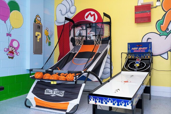 A recreation of a basketball court with a hoop, a bench, and a table with arcade games.