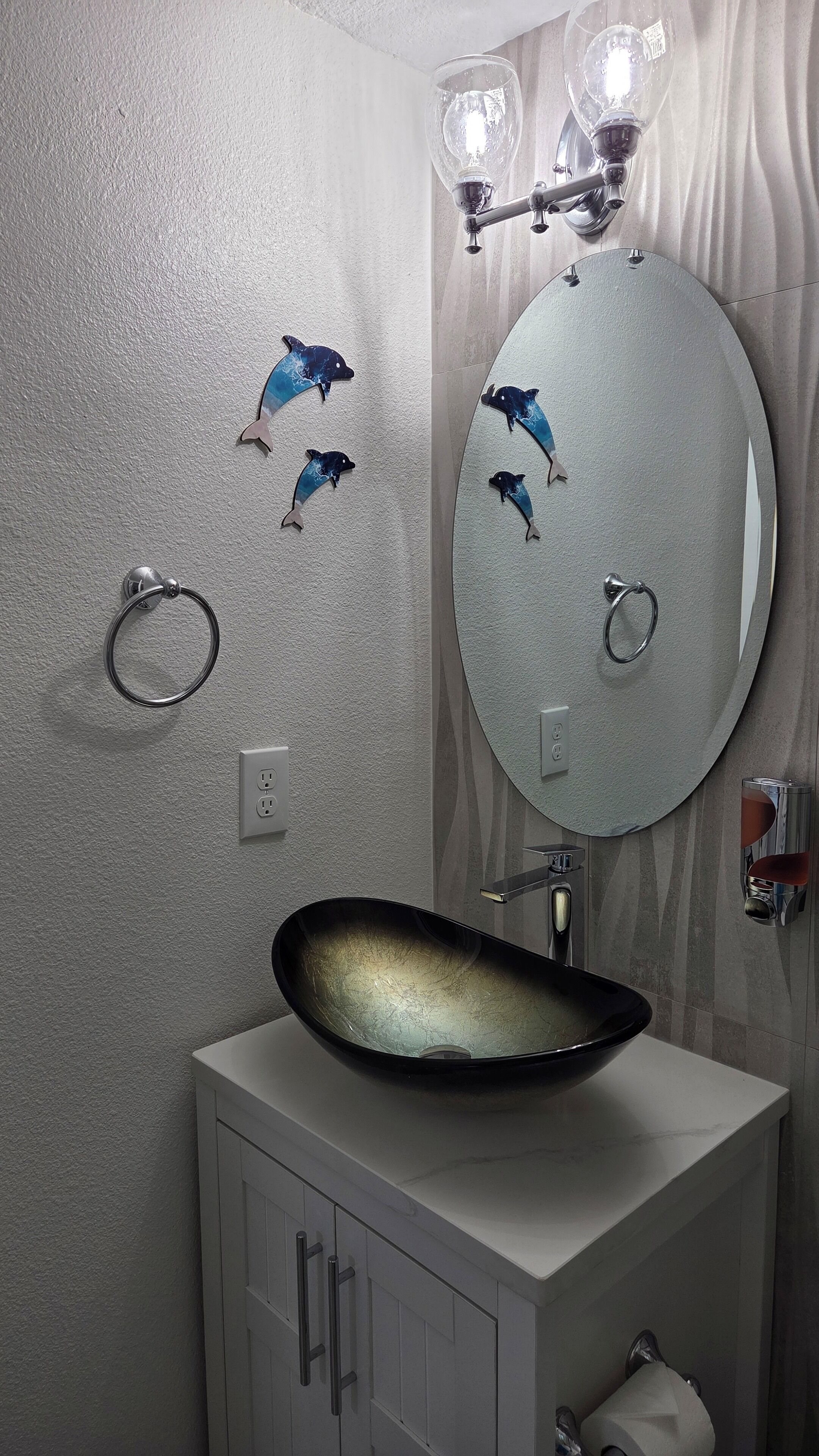 A bathroom with a round mirror, a black vessel sink, and dolphin wall decals.
