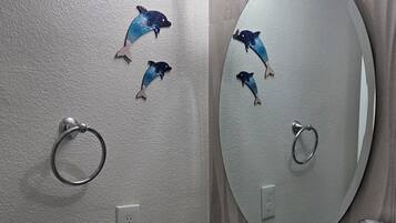 A bathroom with a round mirror, a black vessel sink, and dolphin wall decals.