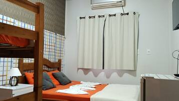 Habitación individual con una cama nido de madera, una mesita de noche con lámpara, una ventana con cortinas y un televisor montado en la pared.