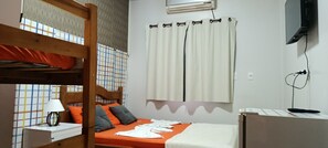 Une chambre avec un lit simple et un lit superposé en bois, une table de chevet avec une lampe, une fenêtre avec des rideaux et un téléviseur fixé au mur.