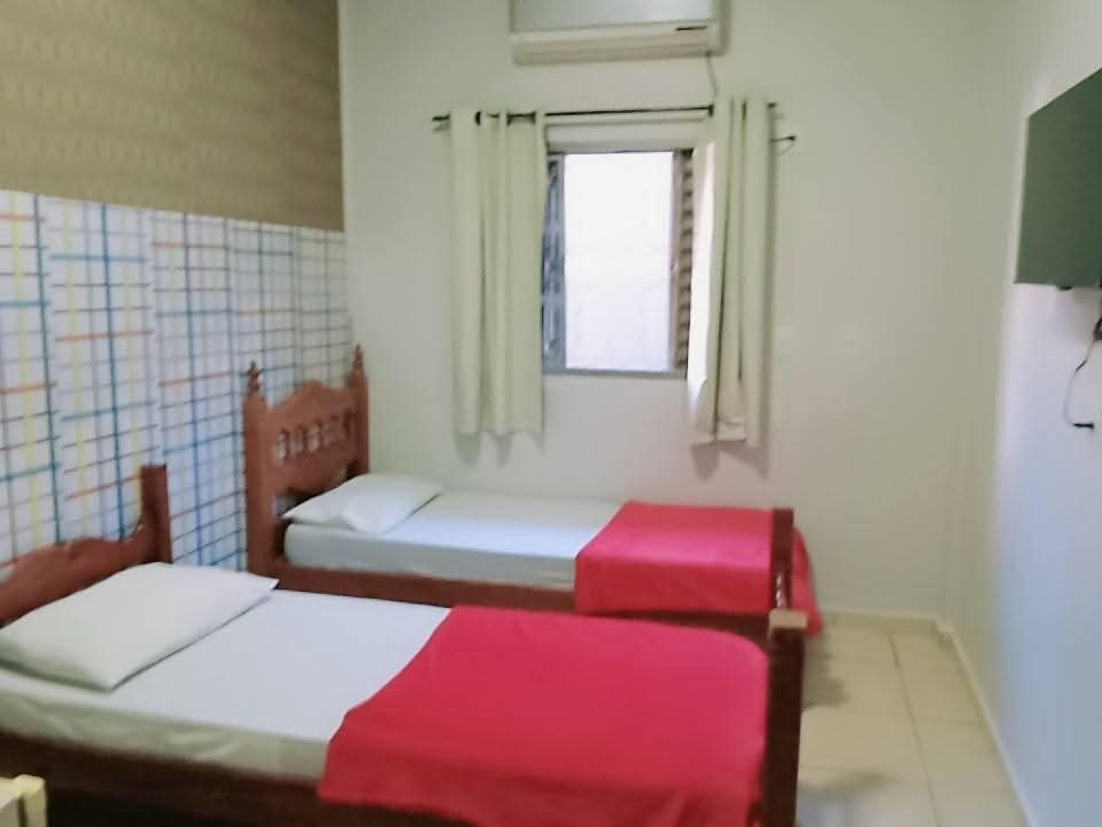 Una habitación pequeña con dos camas individuales, una ventana con cortinas y un aire acondicionado instalado en la pared.