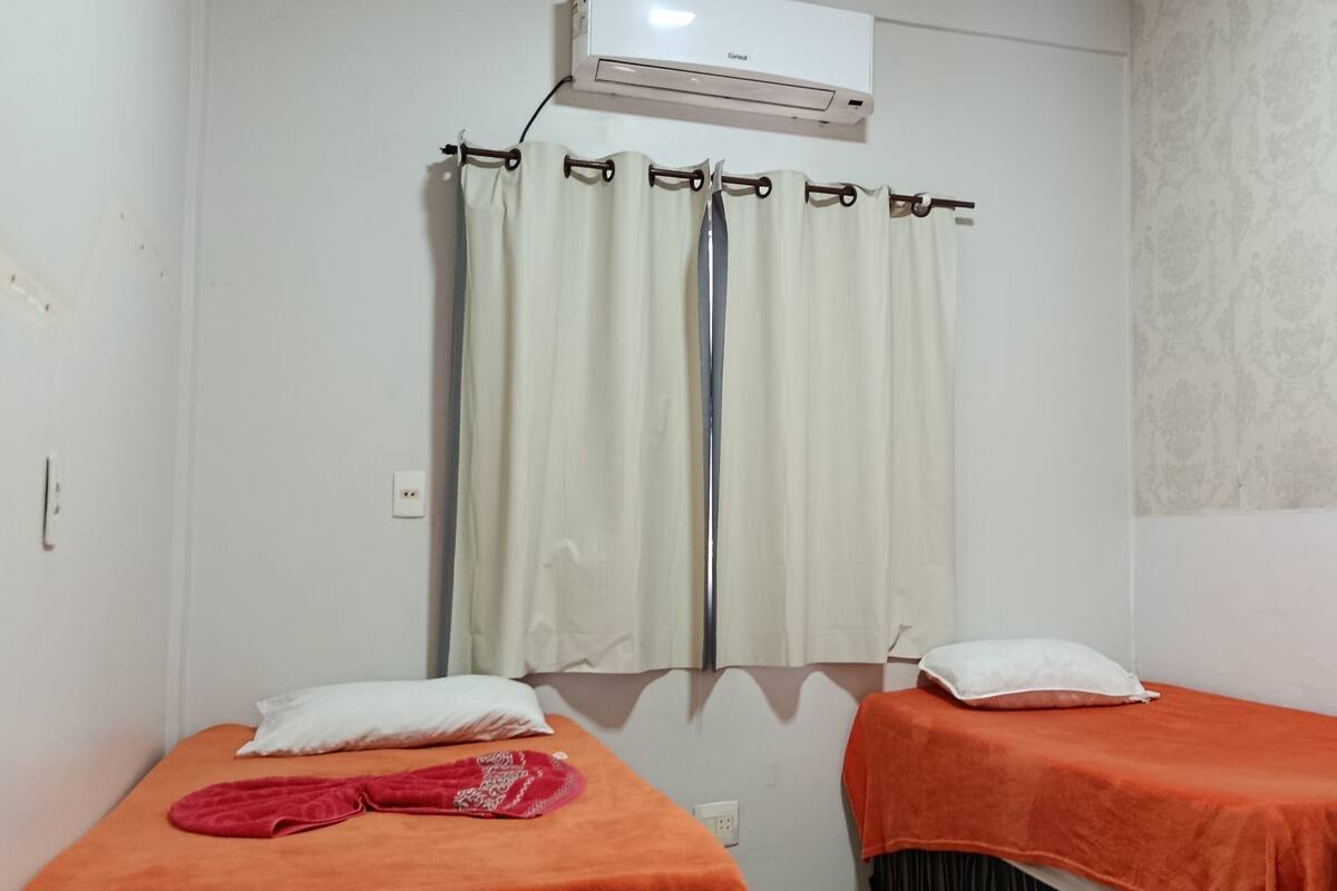 Une chambre avec deux lits, une fenêtre avec des rideaux, un appareil de climatisation et un mur décoré de motifs.
