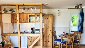 A compact kitchen with wooden cabinetry, a coffee maker, and a toaster. There are two wooden chairs with blue cushions around a small table. - Apartment Emma by Interhome (Trassenheide)