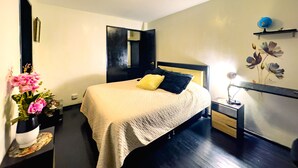 A bedroom with a bed, a nightstand, a vase with flowers, a mirror, and a wall with a floral mural. - Downtown private apartment (Bogotá)