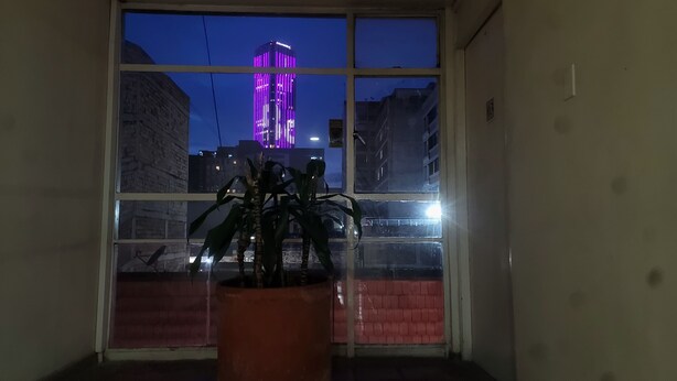 A window with a view of a building with purple lights, a potted plant, and a brick wall. - Downtown private apartment (Bogotá)