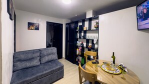 A compact living space with a grey sofa, a wooden dining table, and a black shelving unit against the wall. - Downtown private apartment (Bogotá)