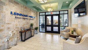 A lobby with a stone wall, a reception desk, two sofas, and a TV mounted on the wall. - 10BR/5BA Retreat • Private Pool • Free Clubhouse Access-4573TB (Kissimmee)
