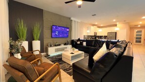 A modern living room with a flat-screen TV, black leather sofas, a white coffee table, and a wooden chair. - 10BR/5BA Retreat • Private Pool • Free Clubhouse Access-4573TB (Kissimmee)