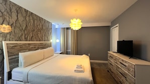A modern hotel room with a large bed, a wooden headboard, a television on a dresser, and a marble-patterned wall. - 10BR/5BA Retreat • Private Pool • Free Clubhouse Access-4573TB (Kissimmee)