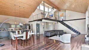 Un loft spacieux avec de hauts plafonds, une cuisine équipée d’appareils modernes, un coin repas, un salon avec un canapé d’angle et un escalier menant à un niveau supérieur.