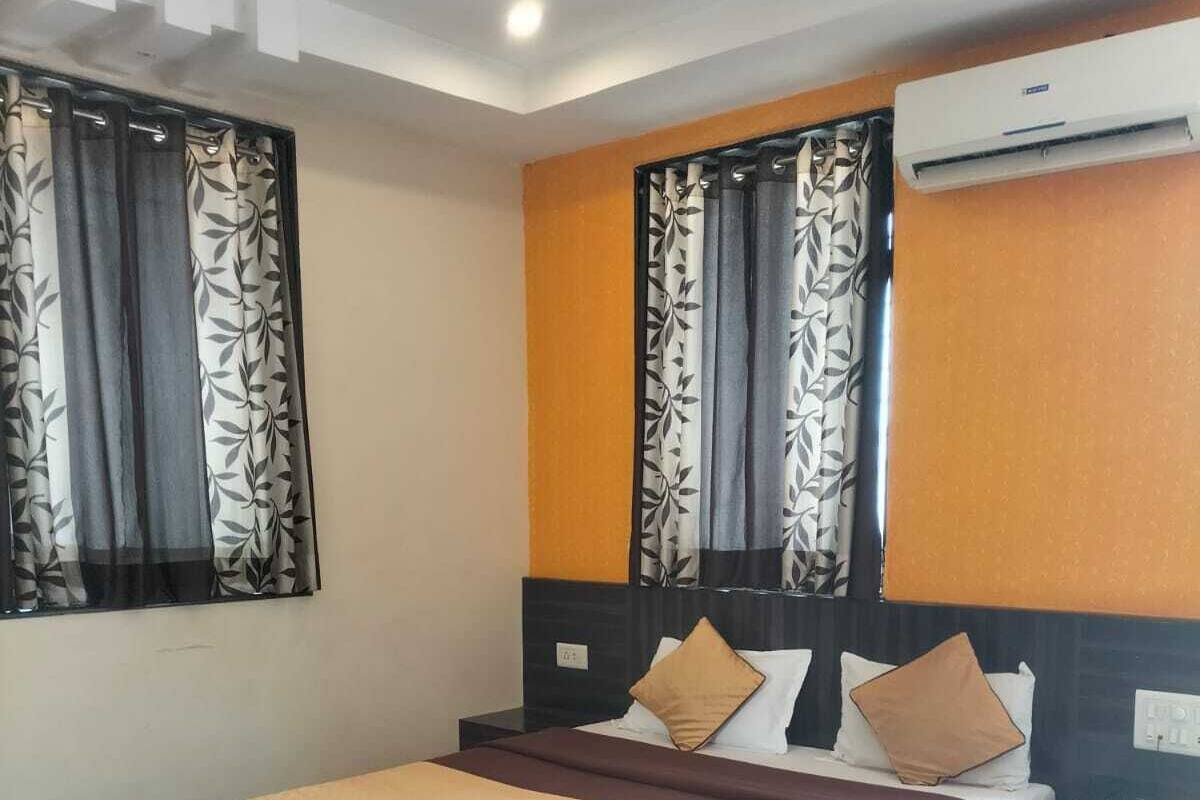Une chambre d’hôtel avec un grand lit, une table de chevet, un appareil de climatisation et une fenêtre avec des rideaux à motifs.