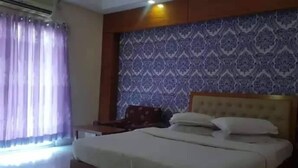 Een hotelkamer met een bed, nachtkastje, houten hoofdeinde en een behang met patroon.