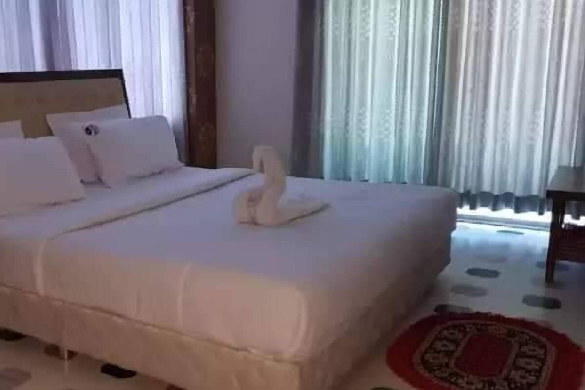 Una habitación de hotel con una cama grande, una mesita de noche y una ventana con cortinas.