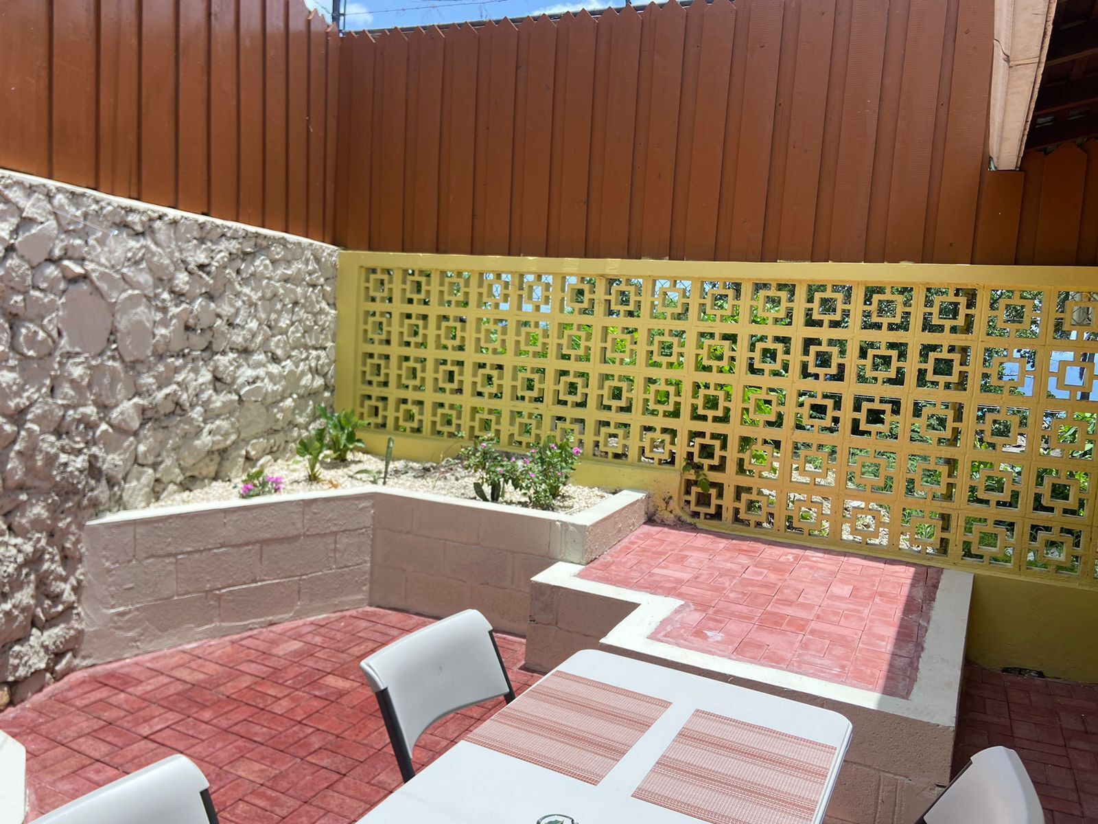 Un'area patio con un muro in pietra, una recinzione in legno e un pavimento piastrellato.