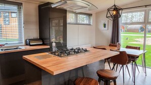 Une cuisine moderne dotée d’un îlot central, d’une cuisinière à gaz et d’une fenêtre avec des stores.