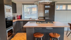 Une cuisine moderne dotée d’un îlot central, d’un four encastré et d’une fenêtre avec stores.