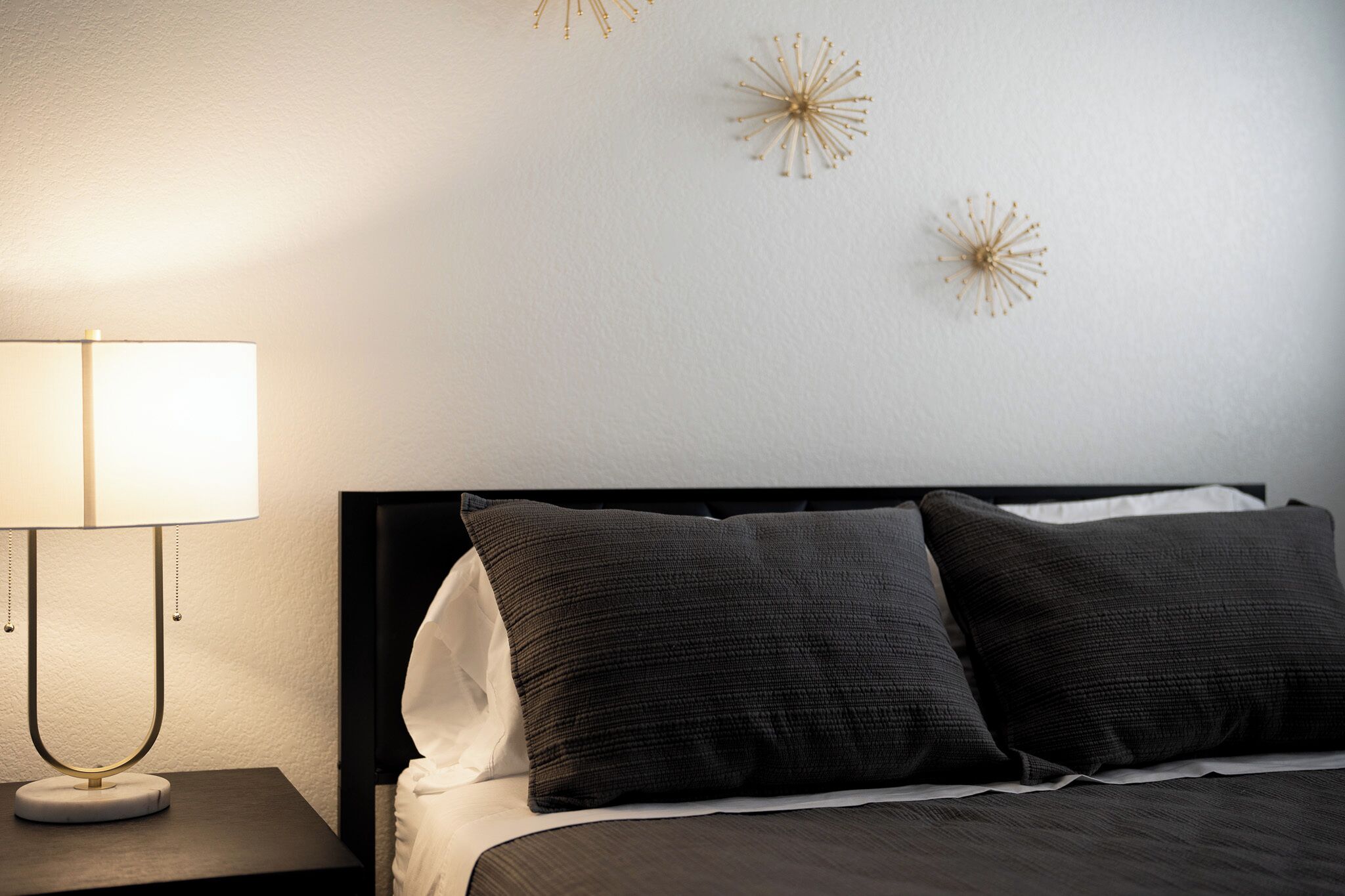 A neatly made bed with dark bedding, a bedside lamp, and decorative wall art.