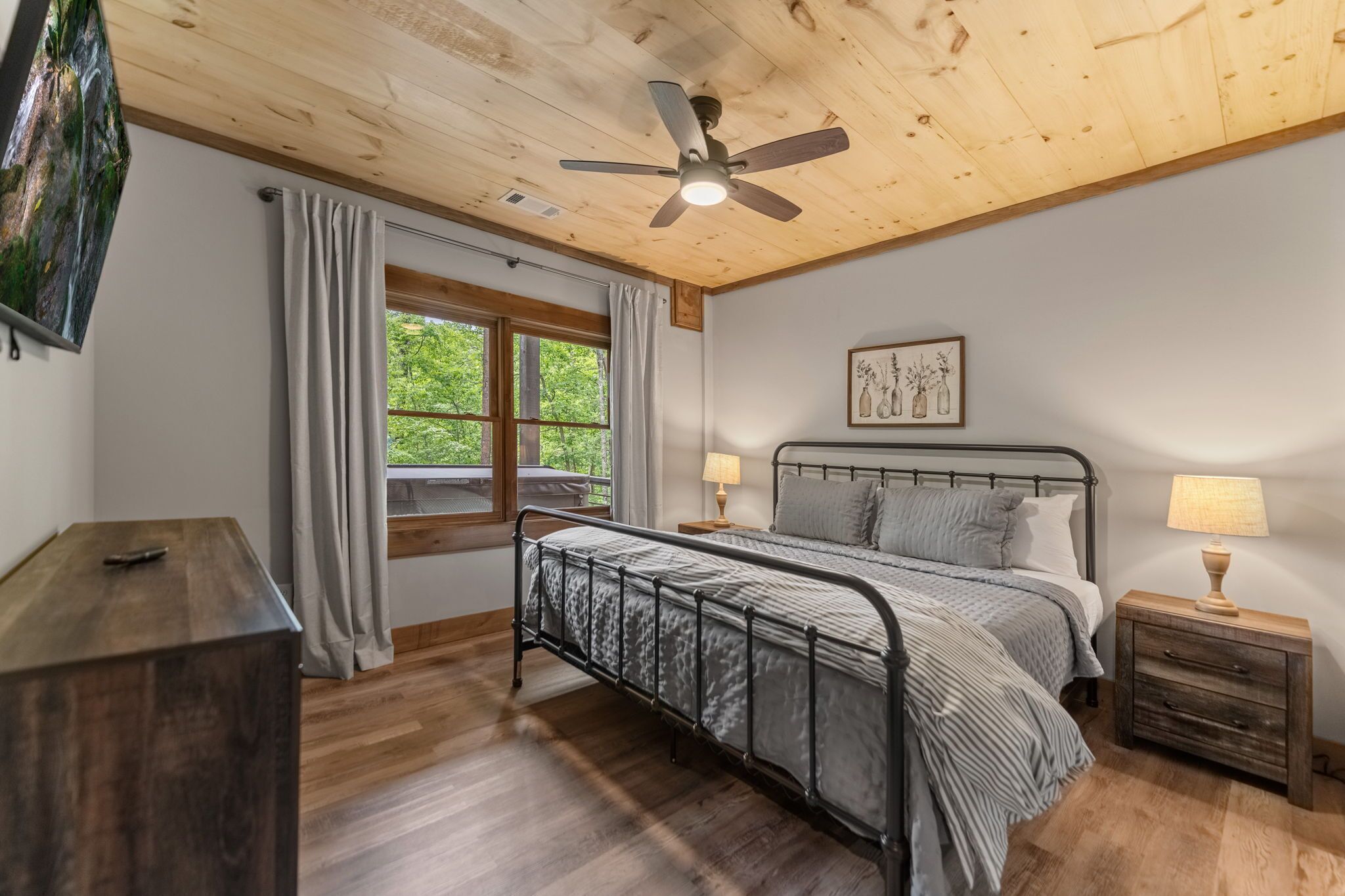 A bedroom with a bed, wooden ceiling, window, and a painting on the wall.