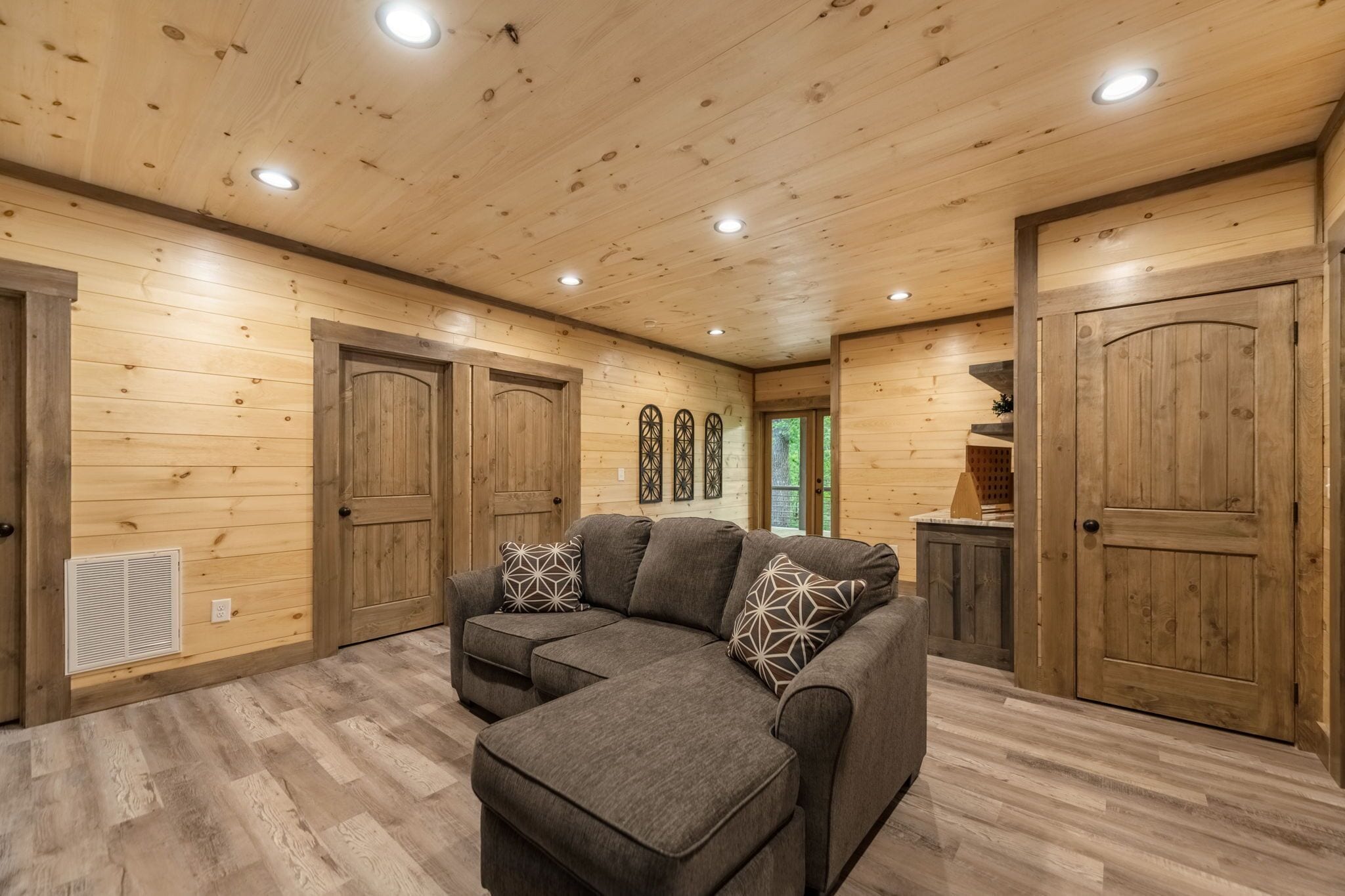 A log cabin interior with a sectional sofa, wooden walls, and a ceiling with recessed lighting.