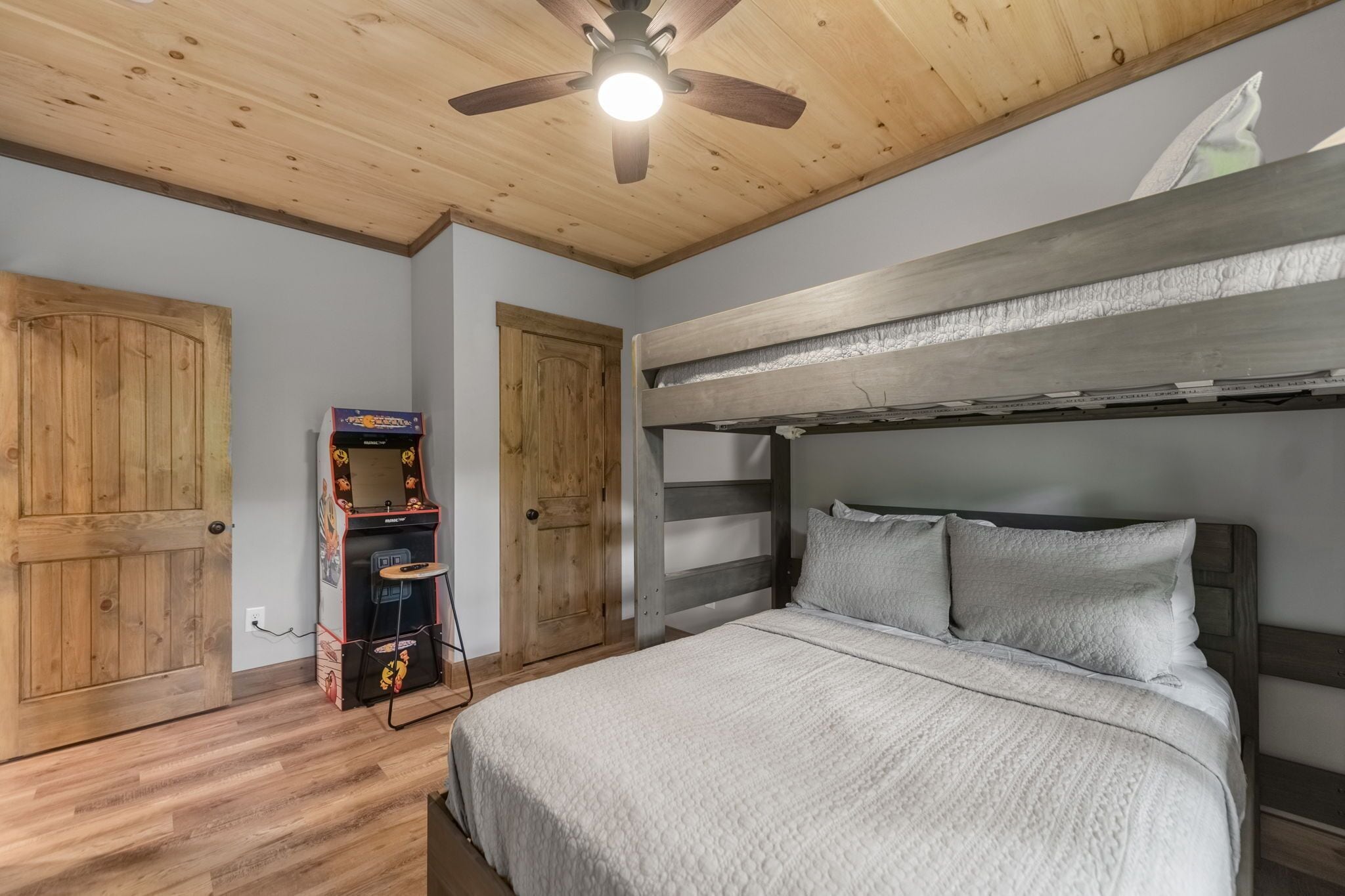A bedroom with a bunk bed, wooden ceiling, and a ceiling fan.