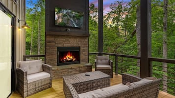 Une terrasse extérieure aménagée avec des meubles en osier, une cheminée en pierre et un téléviseur fixé au-dessus.