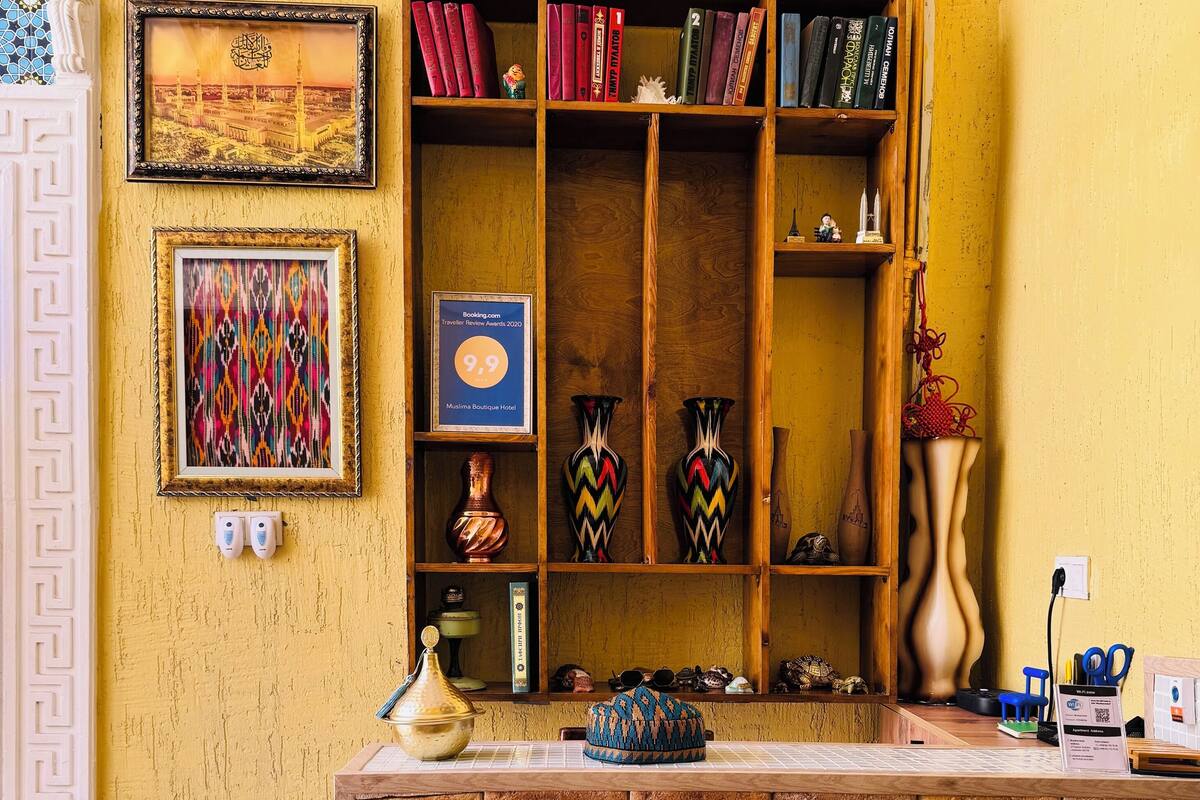 A reception area with a wooden desk, a bookshelf with books and decorative items, a framed award, and a patterned wall.