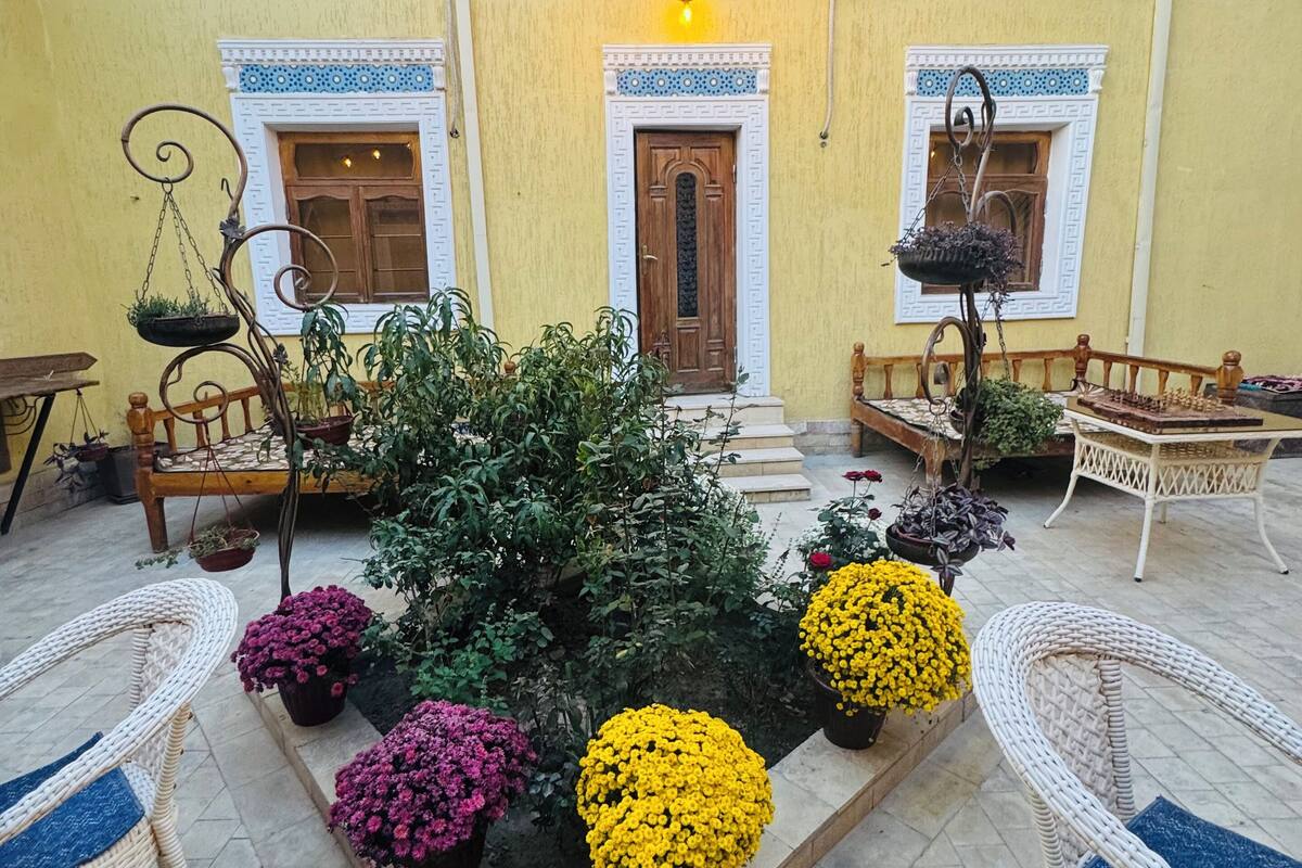 A courtyard with a central planter box containing various flowers, surrounded by wicker furniture and a wooden bench.