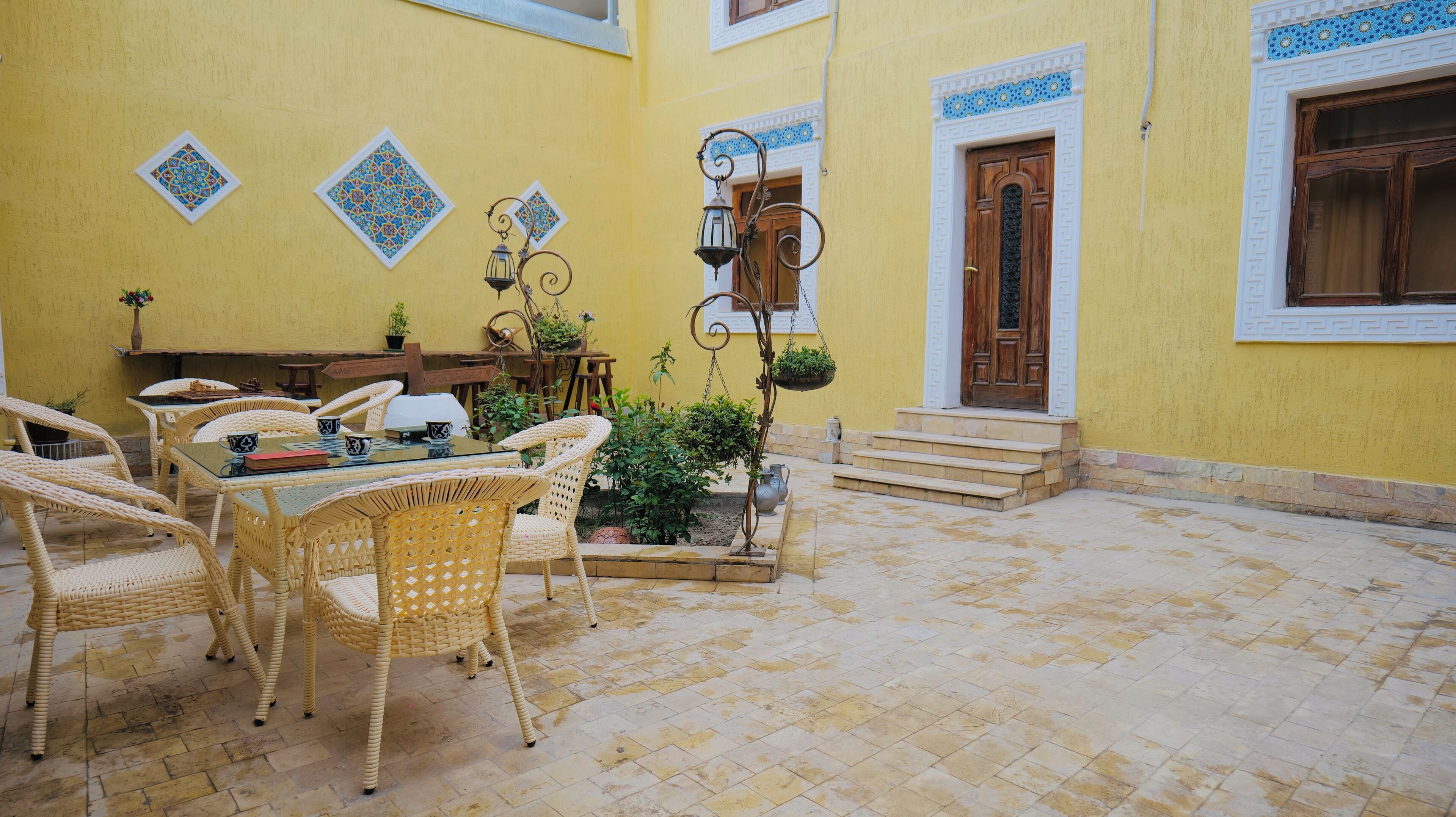 A yellow-walled courtyard with wicker furniture, a table, and a hanging lantern.