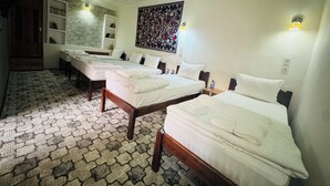 Egy három egyágyas ággyal rendelkező szállodai szoba, mintás padlóval, egy nagy faliszőnyeggel és egy fa ajtóval.