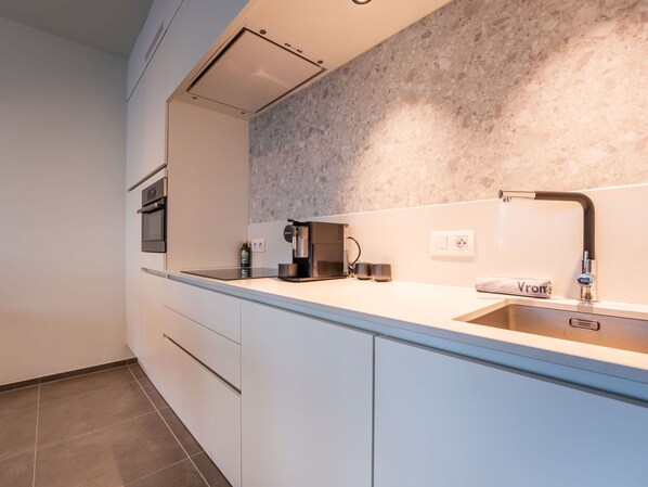 A modern kitchen with a built-in oven, a coffee maker, and a sink with a towel labeled "Vroom".