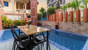 A pool area with a tiled floor, a wooden table with chairs, and potted plants. - 855 Villa Siem Reap  (Siem Reap)