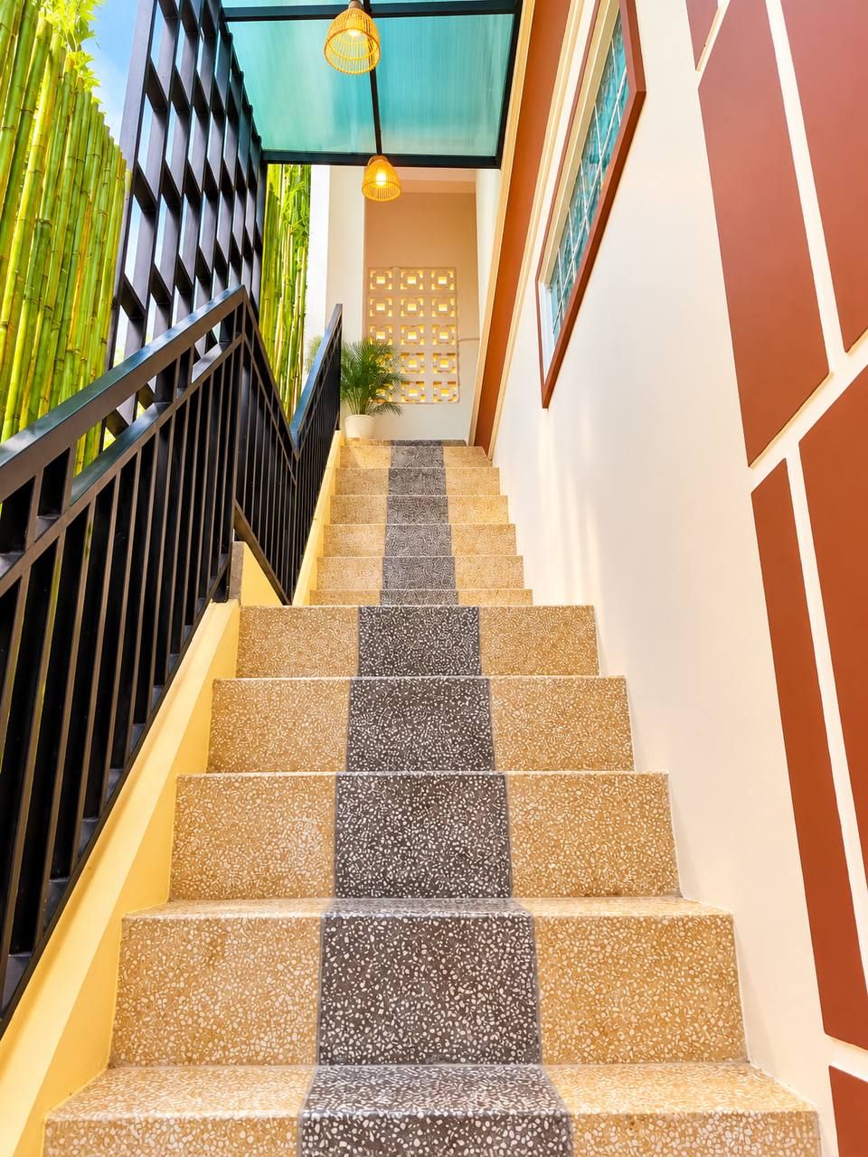 A staircase with alternating beige and dark tiles, a black railing, and a wall with a geometric pattern.