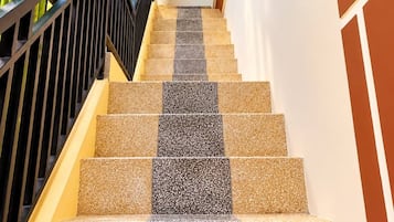 A staircase with alternating beige and dark tiles, a black railing, and a wall with a geometric pattern.