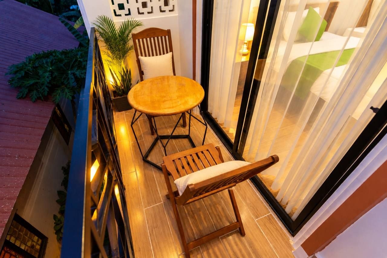 A small outdoor seating area with a table and chairs, a potted plant, and a view of a building with a geometric facade.