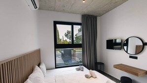 A modern hotel room with a large bed, a TV, a mirror, and a view of the outdoors.