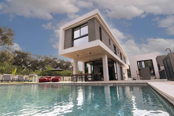 Une maison moderne à deux étages, avec une piscine en premier plan.