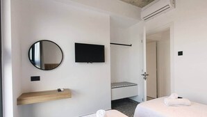 Hotellihuone, jossa on kaksi sänkyä, televisio, peili, puinen hylly ja ovi, joka johtaa toiseen huoneeseen.